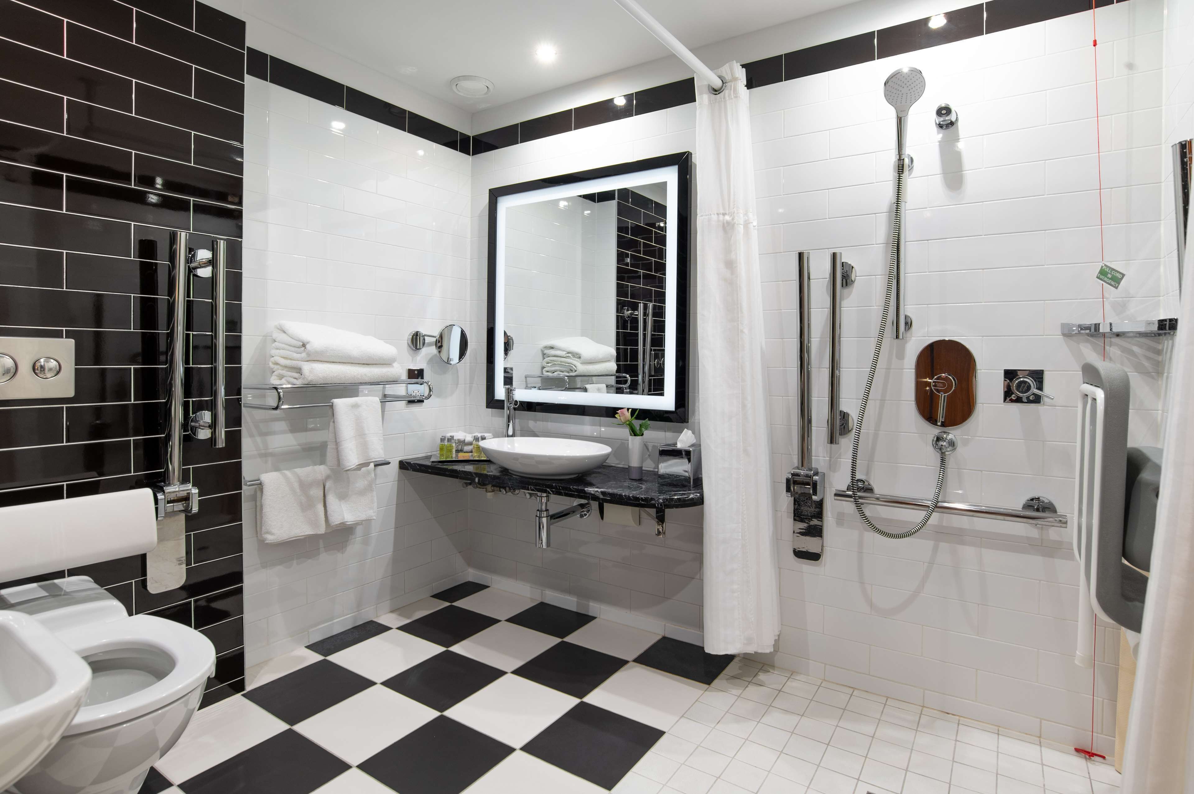 A modern bathroom with a black and white checkered floor, a white sink, a large mirror, and a shower area.