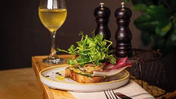 A plate of food with a glass of white wine, a fork, and a knife on a table with a plant and salt and pepper shakers in the background.