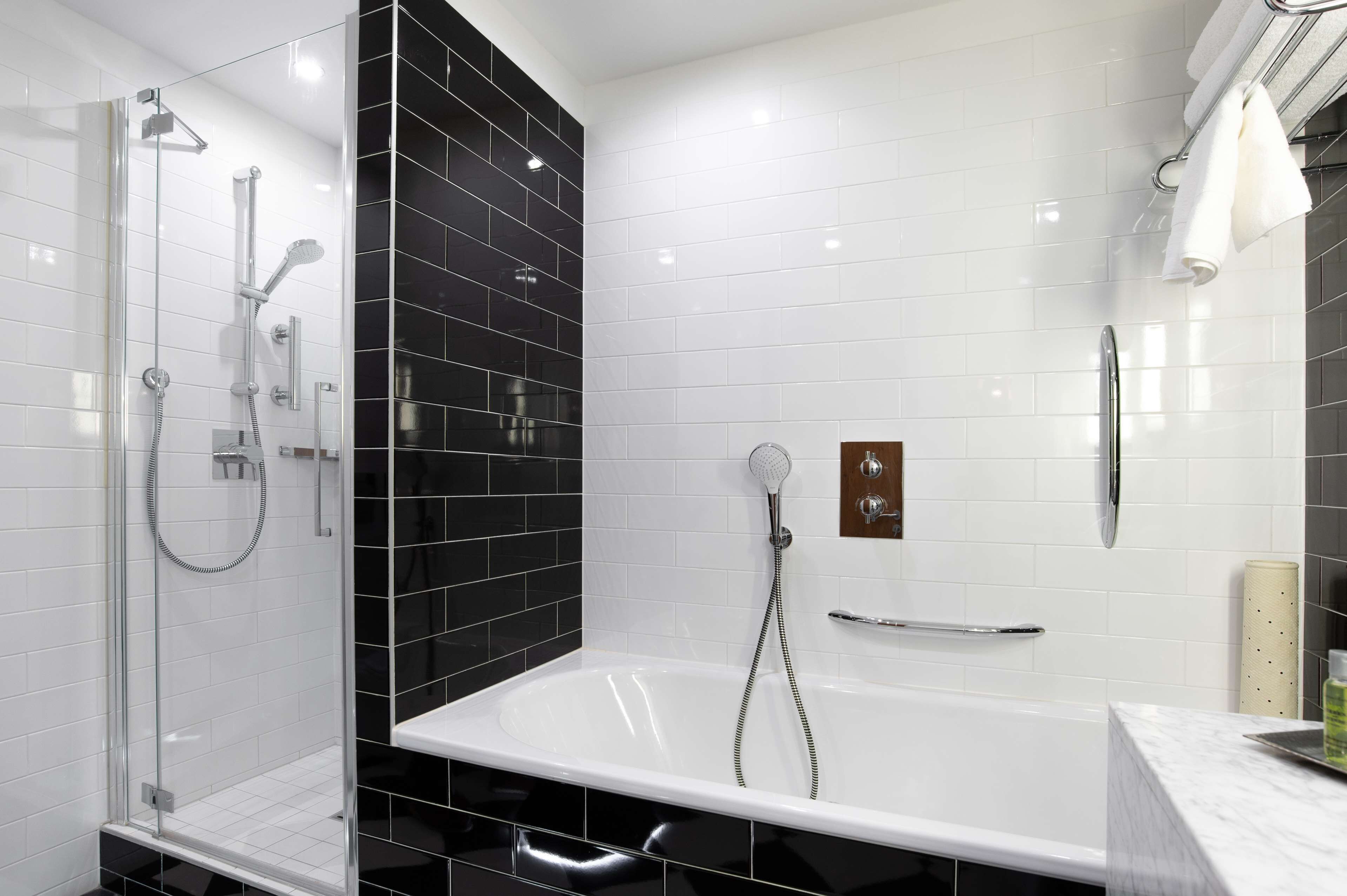 A modern bathroom with a glass-enclosed shower, a white bathtub, and black-tiled walls.