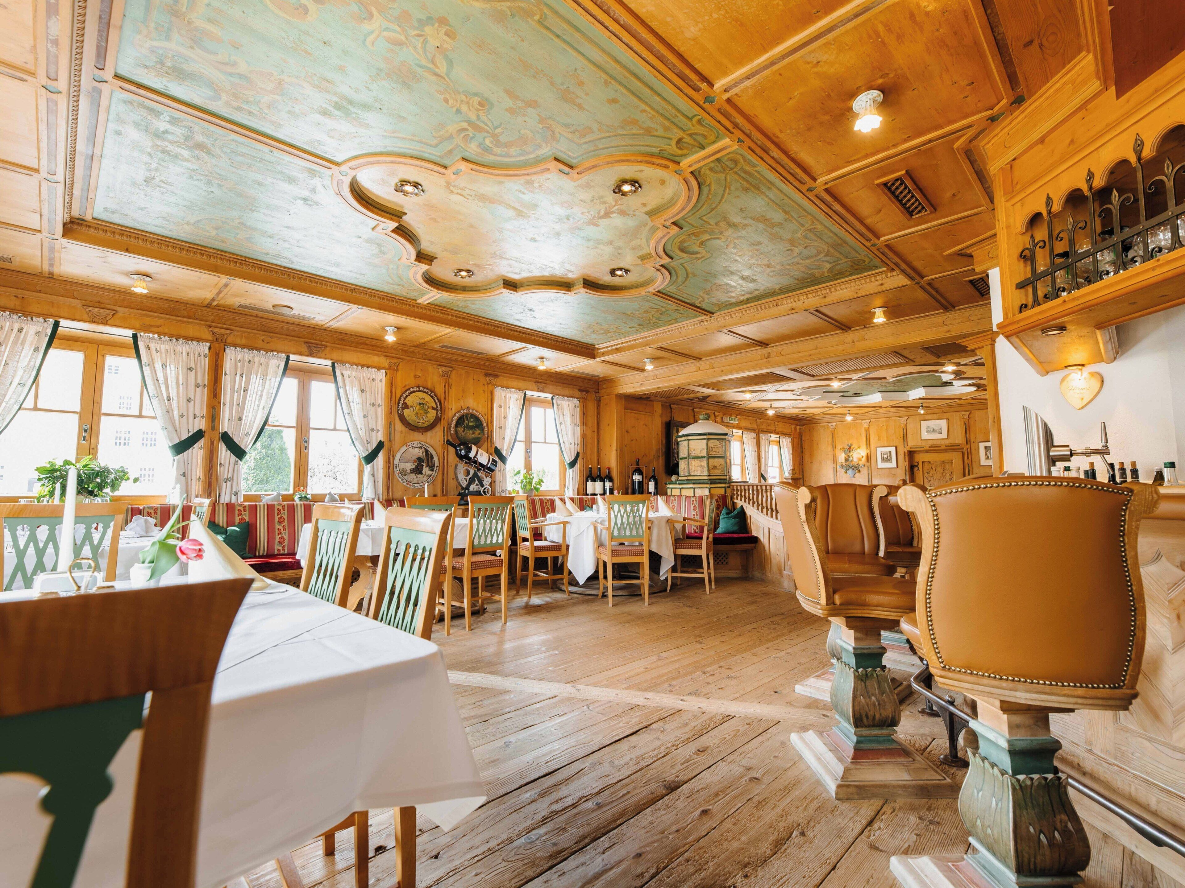 Een traditionele herberg met houten inrichting, waaronder een eetgedeelte met tafels en stoelen, een bar met flessen en een plafond met decoratieve versieringen.
