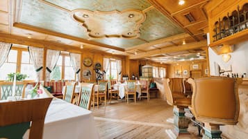 Een traditionele herberg met houten inrichting, waaronder een eetgedeelte met tafels en stoelen, een bar met flessen en een plafond met decoratieve versieringen.