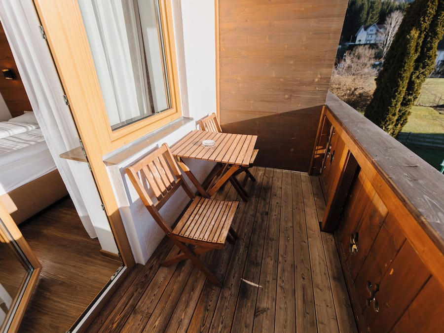 Een houten terras met een tafel en stoelen, een raam en uitzicht op een landschap.