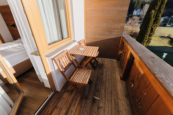 Una terraza de madera con una mesa, sillas, un ventanal y vistas del paisaje.