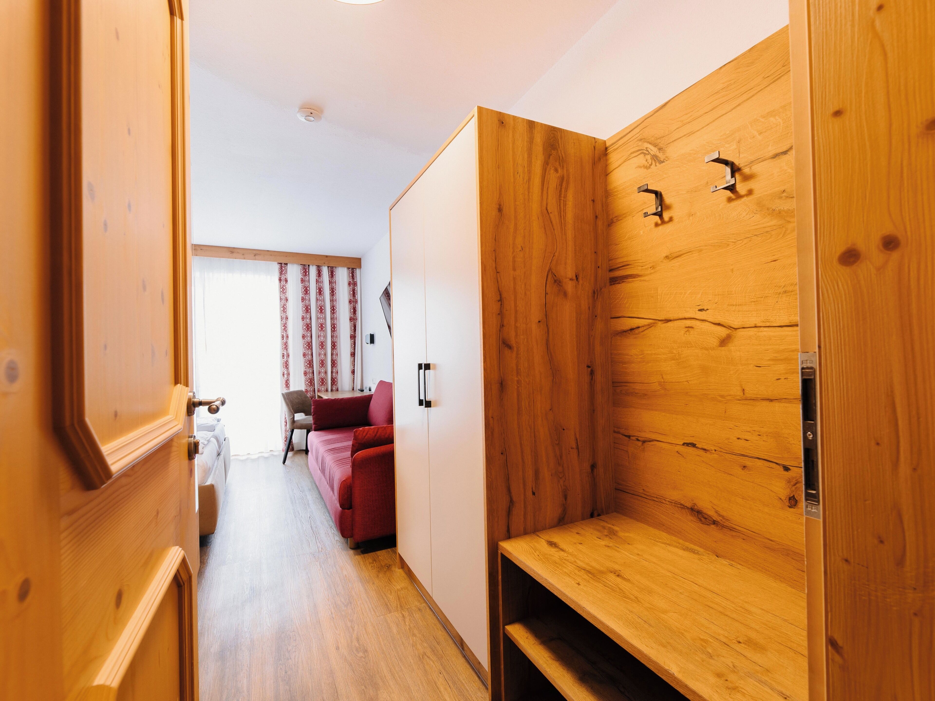 A hallway with a wooden wardrobe, a red sofa, and a wooden bench.
