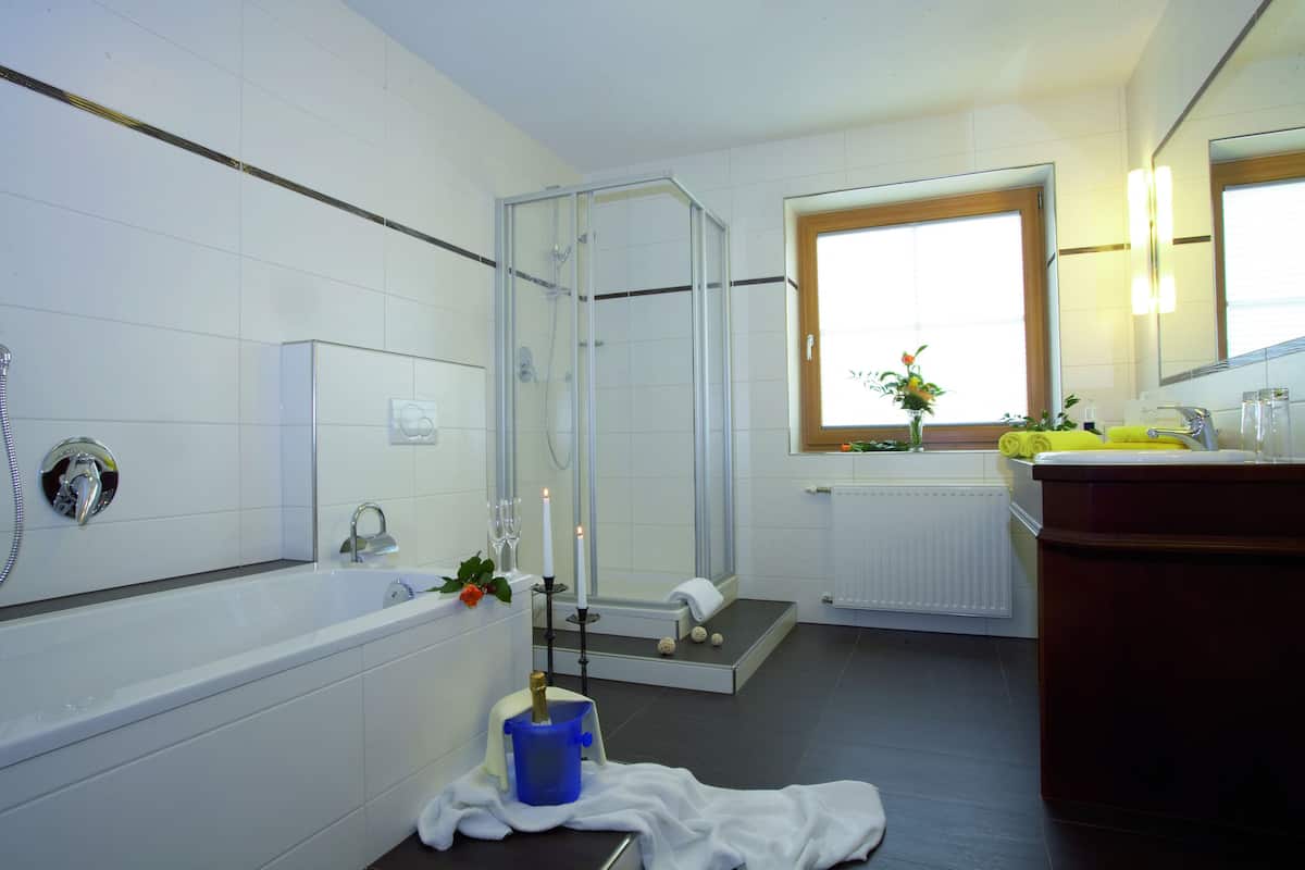A modern bathroom with a glass-enclosed shower, a bathtub, a sink with a mirror, and a window providing natural light.