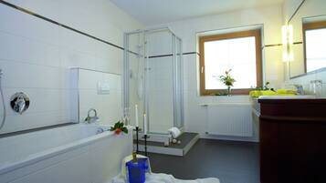 Un baño moderno con ducha envuelta en vidrio, una bañera, un lavabo con espejo y una ventana que proporciona luz natural.