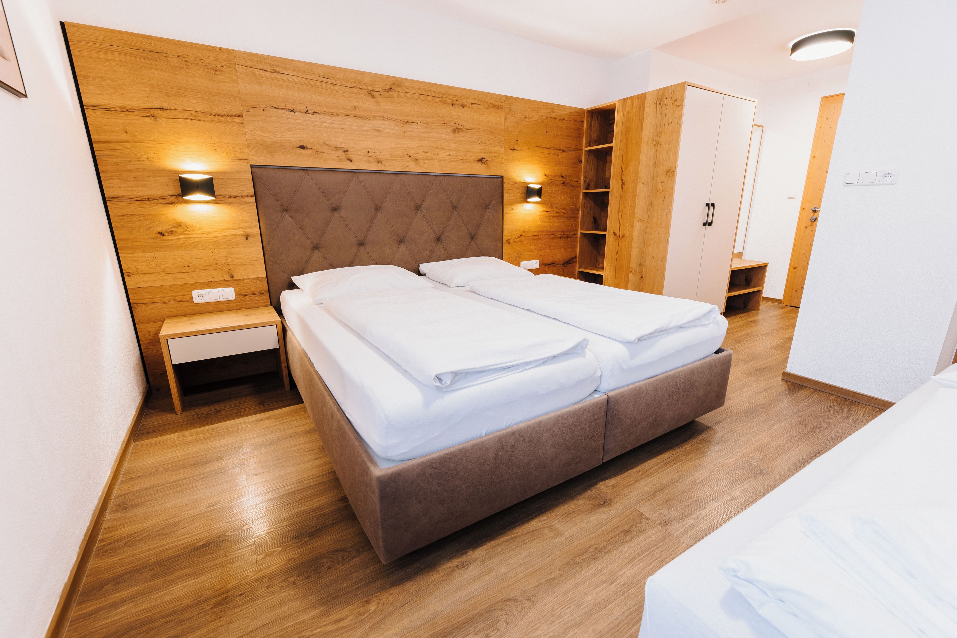 A modern bedroom with a wooden headboard, a bed with white linens, a nightstand, and built-in shelving.