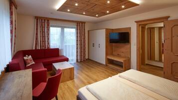 Ein modernes Hotelzimmer mit Holzboden, einem roten Sofa, einem Bett, einem Fernseher und einem Kleiderschrank.