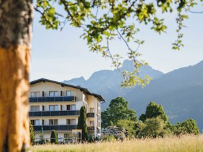 A multi-story building with balconies, surrounded by a grassy field and trees, with mountains in the background. - Alpenhotel Ernberg (Breitenwang)