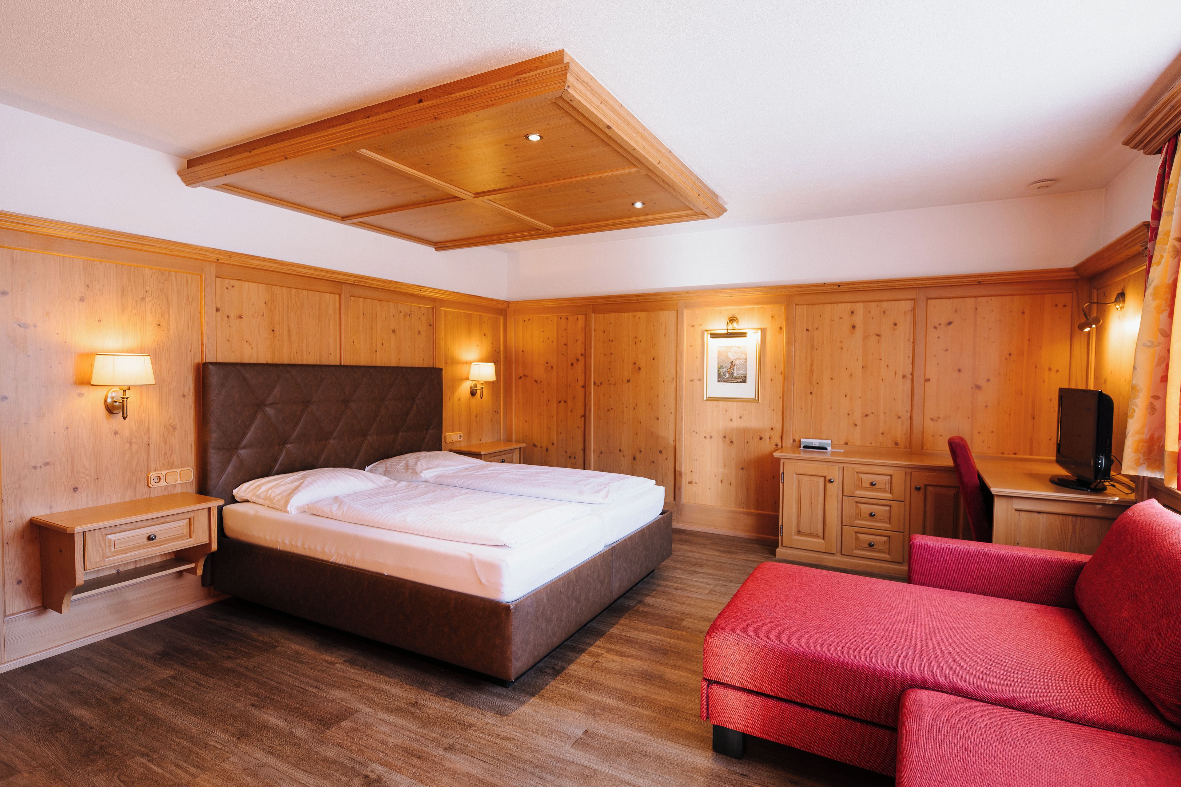 Ein Hotelzimmer mit Holzboden, einem großen Bett, einem Schreibtisch, einem Sessel und einem roten Sofa.