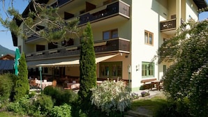 Un hotel de varios pisos con balcones, una zona de estar exterior cubierta y un jardín bien cuidado.