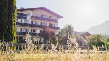 A multi-story building with balconies, surrounded by tall trees and a grassy field.