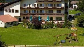 Un hotel de varios pisos con balcón, rodeado de un césped cuidado y un parque infantil.