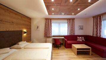 A hotel room with a wooden ceiling, a bed, a red sofa, a desk, and a window with curtains.