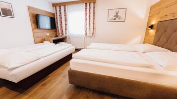 Quarto de hotel com duas camas, cabeceira de madeira, televisão e janela com cortinas estampadas.