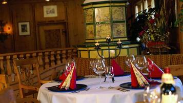 A restaurant setting with a wooden interior, a round table set for two with wine glasses and red napkins, and a candelabra with candles.