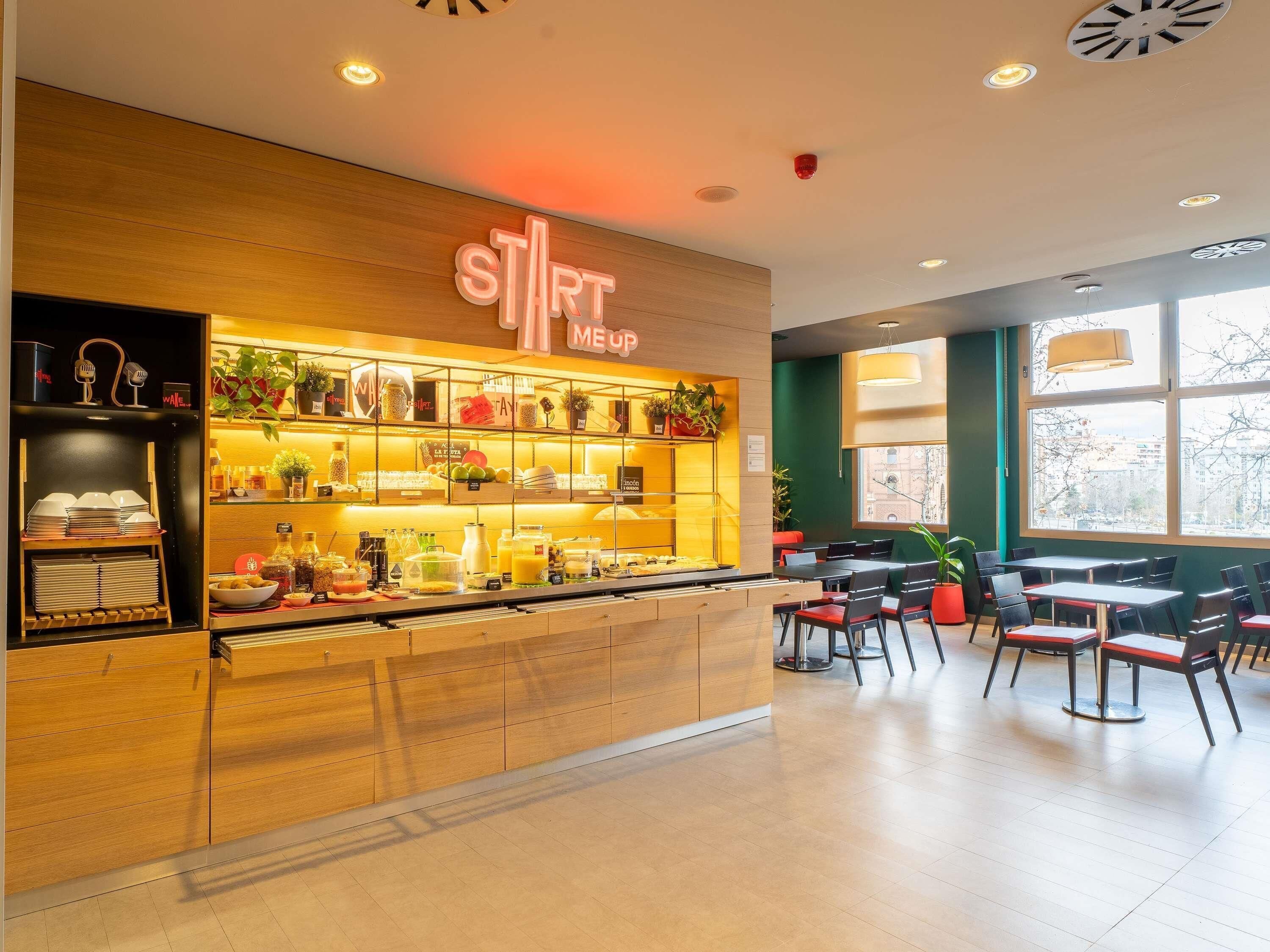 Ein modernes Café mit Holztresen, Regalen voller Speisen und einer Sitzgelegenheit mit Tischen und Stühlen.