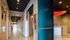 A modern hotel corridor with wooden walls, a teal door, and a reception desk with a red accent.