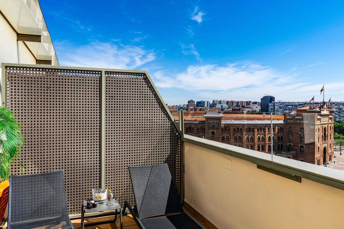 Un balcón con vista a un paisaje urbano, que incluye un edificio histórico con banderas.