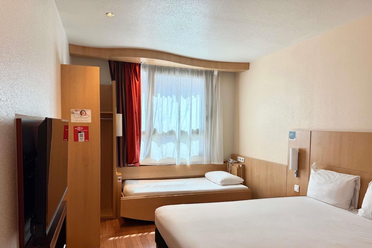 Een hotelkamer met een bed, een televisie, een kledingkast en een raam met gordijnen.