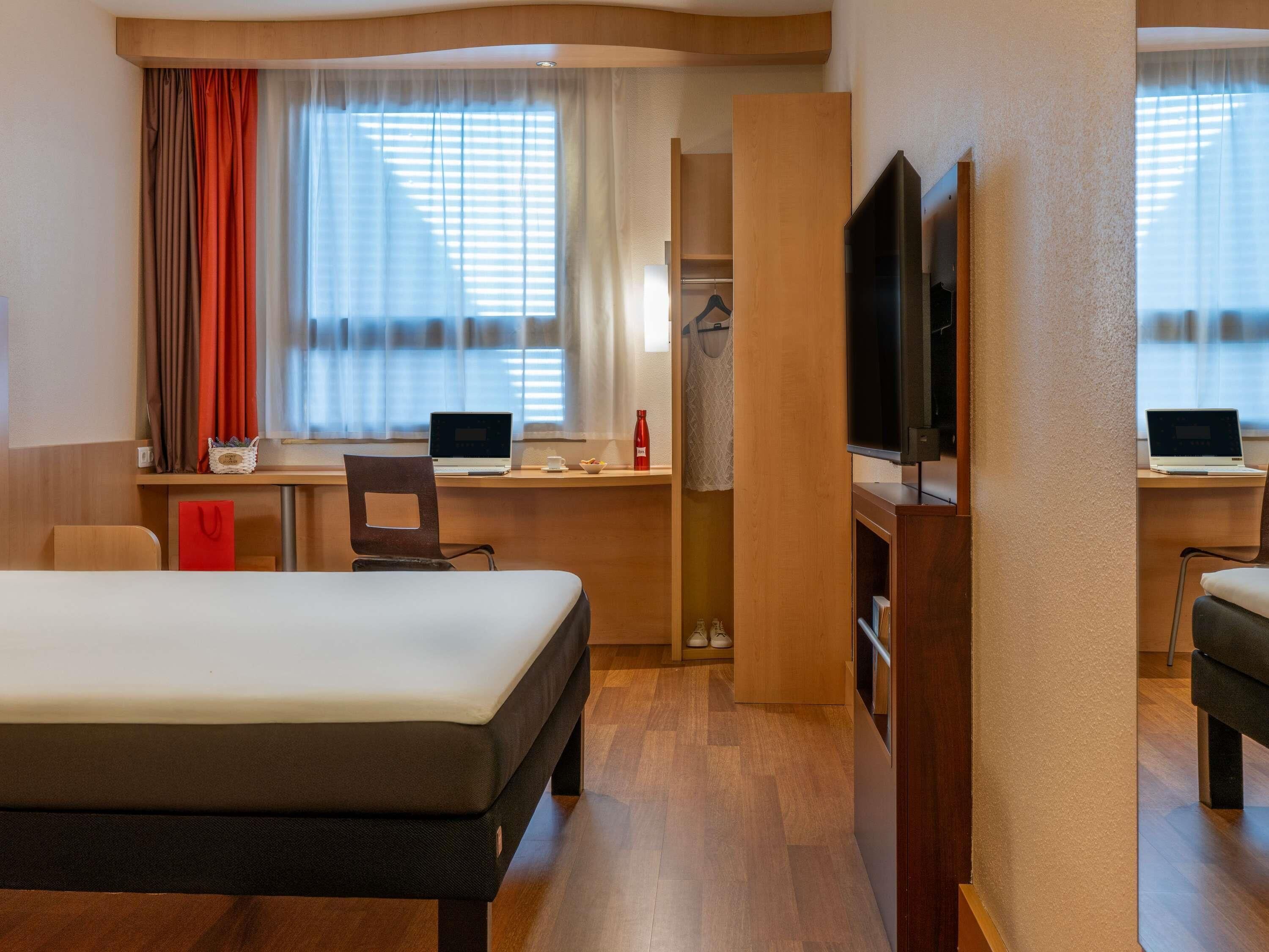 A hotel room with a bed, two desks with laptops, a TV, and a wardrobe.
