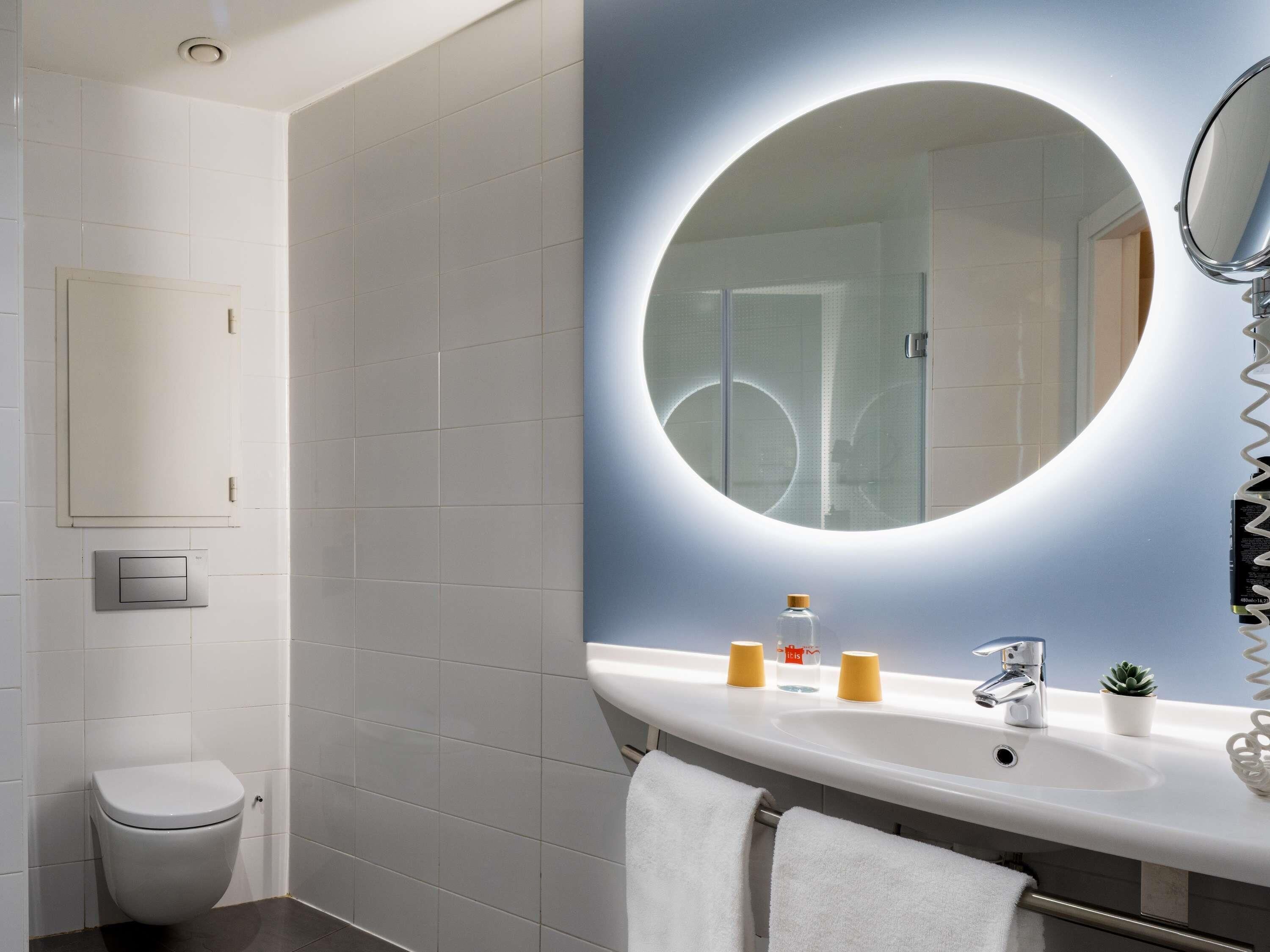 A modern bathroom with a toilet, a sink, a mirror, and a towel rack.