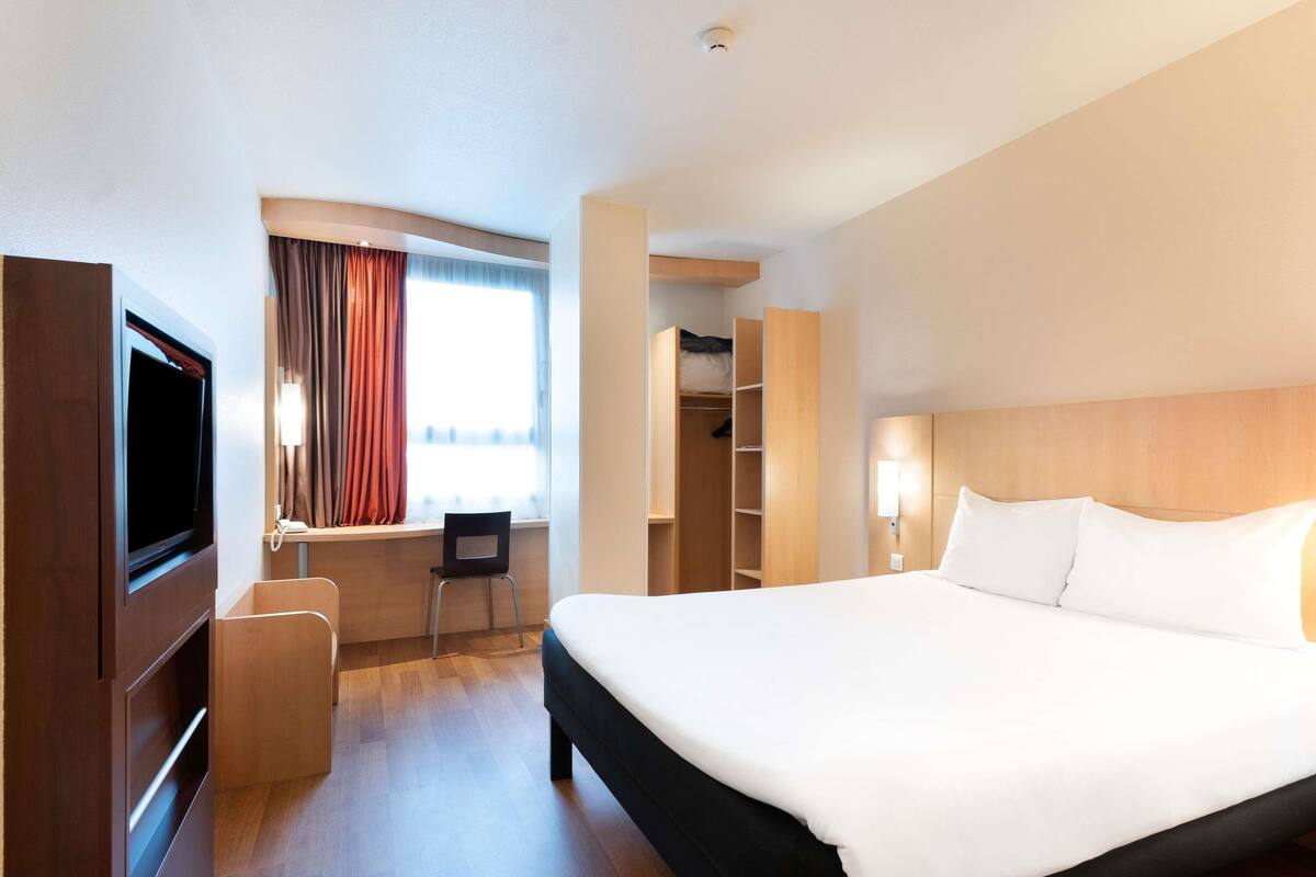 Habitación de hotel con una cama grande, un escritorio con silla, un televisor y un armario.