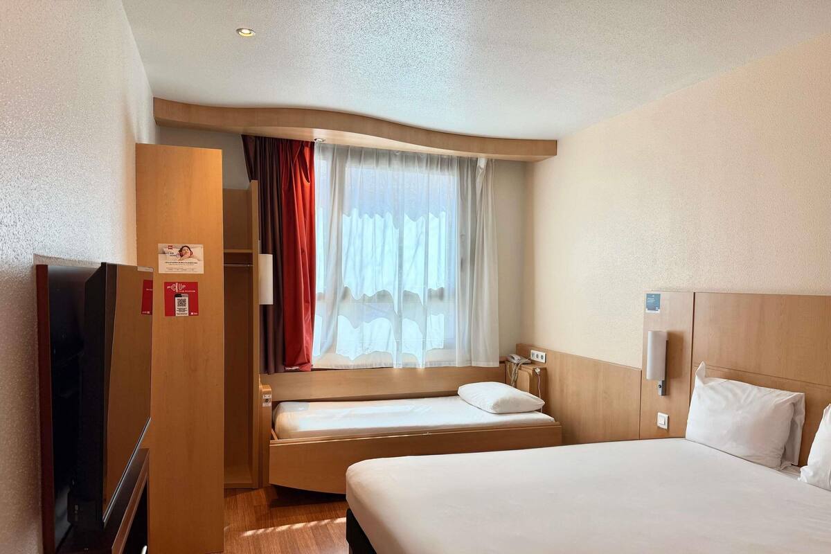 Ein Hotelzimmer mit Bett, Fernseher, Kleiderschrank und einem Vorhangfenster.