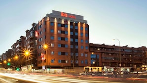 A multi-story hotel with a prominent 'ibis HOTEL' sign, featuring a modern architectural design with a brick facade and multiple balconies.