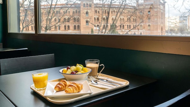 A breakfast tray with croissants, fruit, orange juice, and coffee on a table by a window with a view of a building.