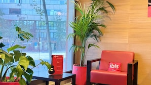 A modern hotel lobby with a red sofa, a large potted plant, and a black table with a red sign.