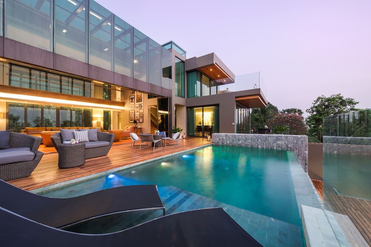 A modern outdoor pool area with lounge chairs, a wooden deck, and a glass-enclosed building.