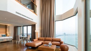 Habitació d'hotel moderna amb una finestra gran, un sofà, zona de menjador i vista a l'aigua.