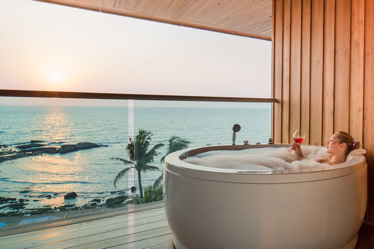 A person relaxing in a large bathtub with a view of the ocean and a sunset.