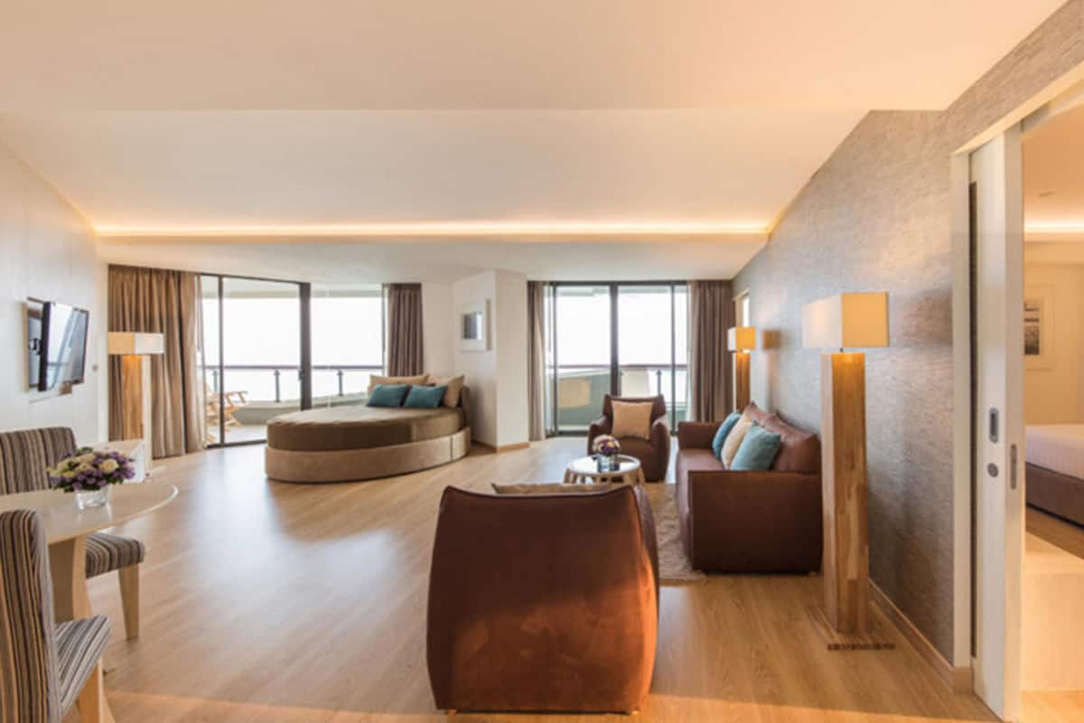 A modern hotel room with a large seating area, a sofa, a coffee table, and a bed.