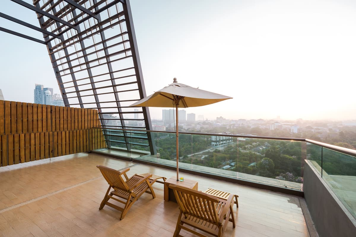 A balcony with wooden flooring, two wooden chairs, a table, and a large umbrella.