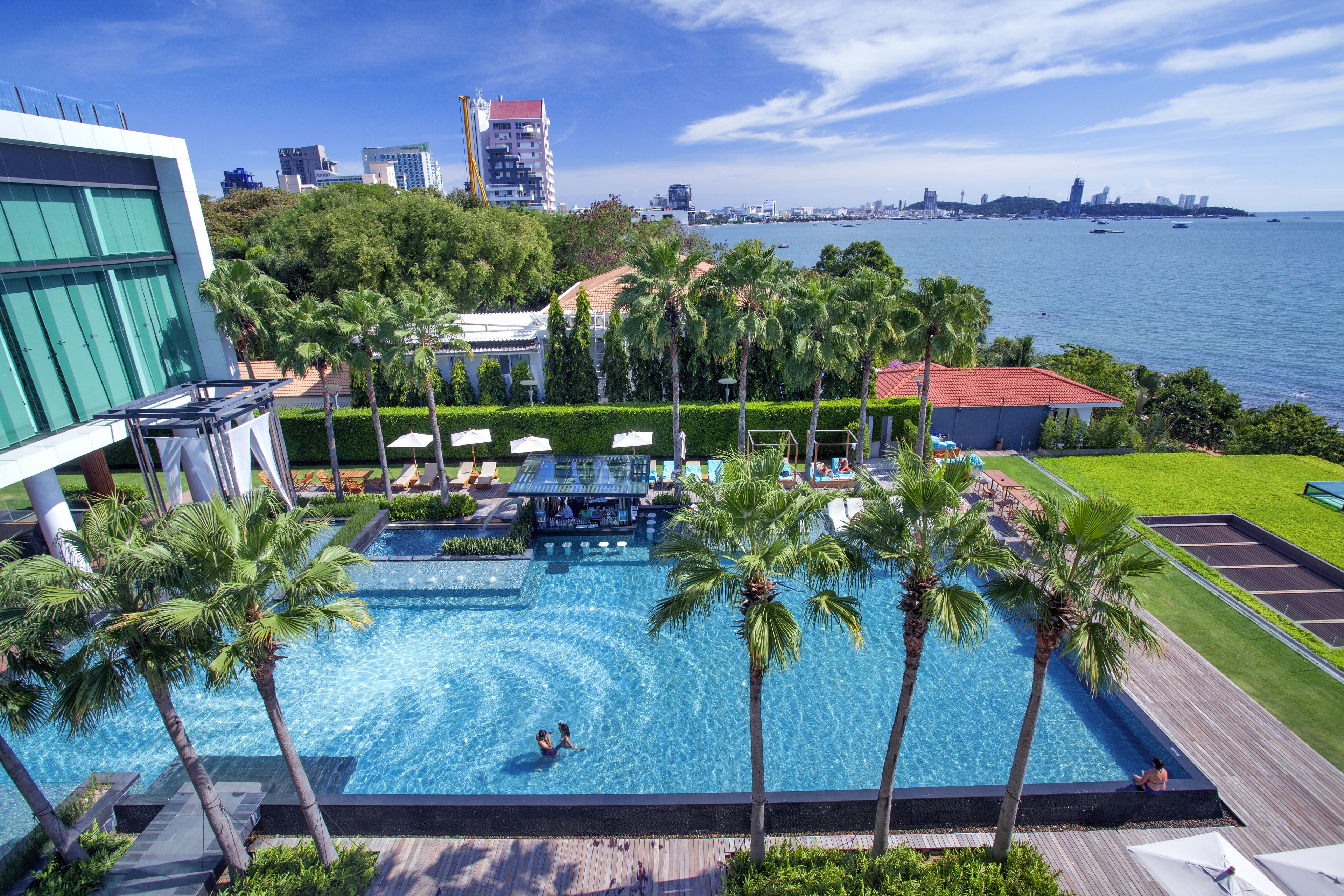 A rooftop pool with palm trees, a bar, and a view of the city skyline.
