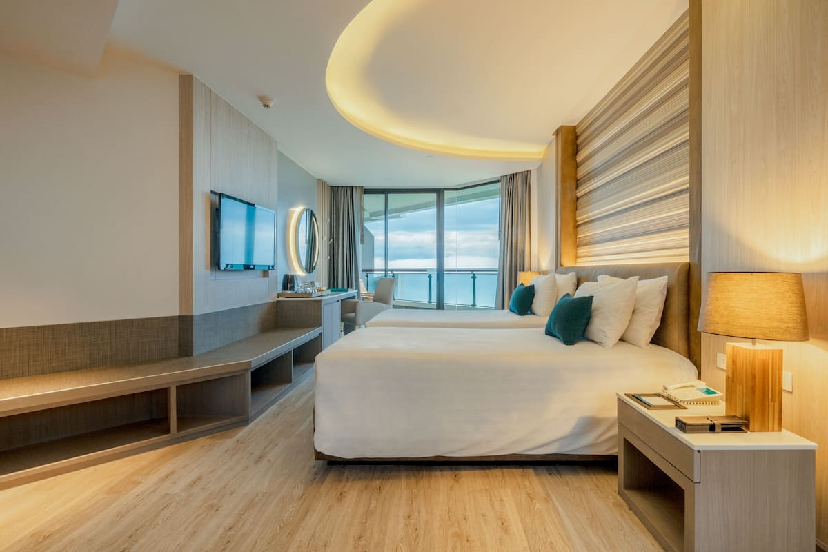 A modern hotel room with a large bed, a desk, a TV, and a view of the sky.