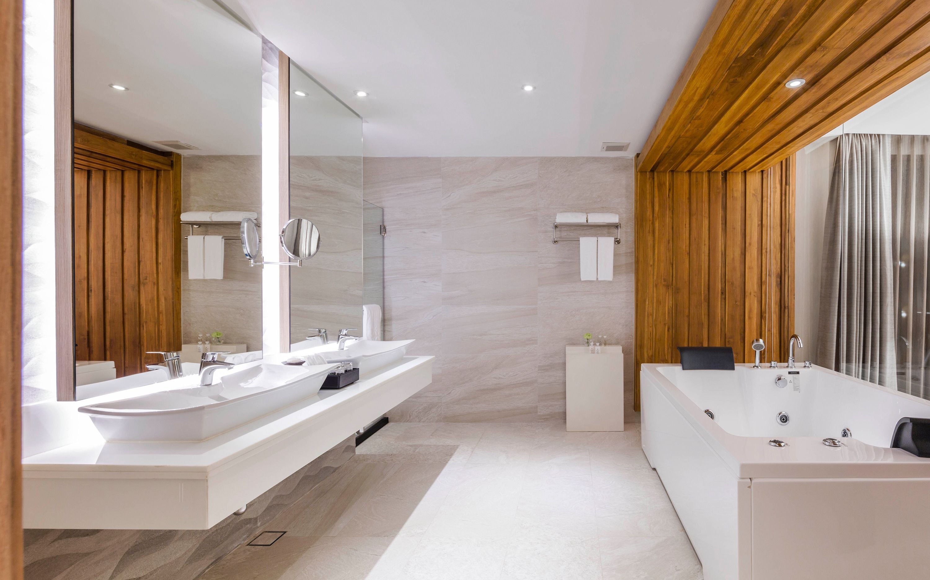 A modern bathroom with two sinks, a large bathtub, wooden paneling, and a large mirror.
