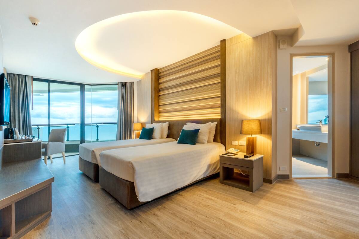 A modern hotel room with two beds, a desk, and a view of the sky.