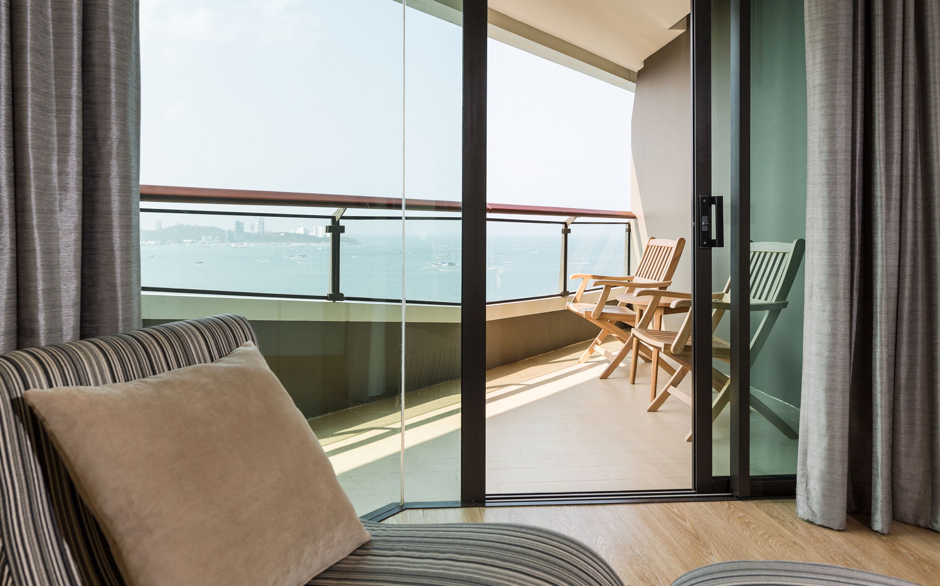 A balcony with a view of the sea, a sofa, and wooden chairs.