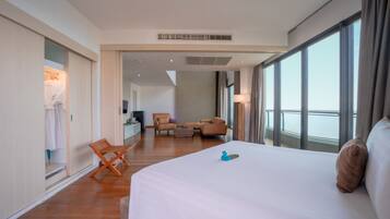 A hotel room with a large bed, a seating area with a sofa and chairs, a small table, and a view of the outside through large windows.