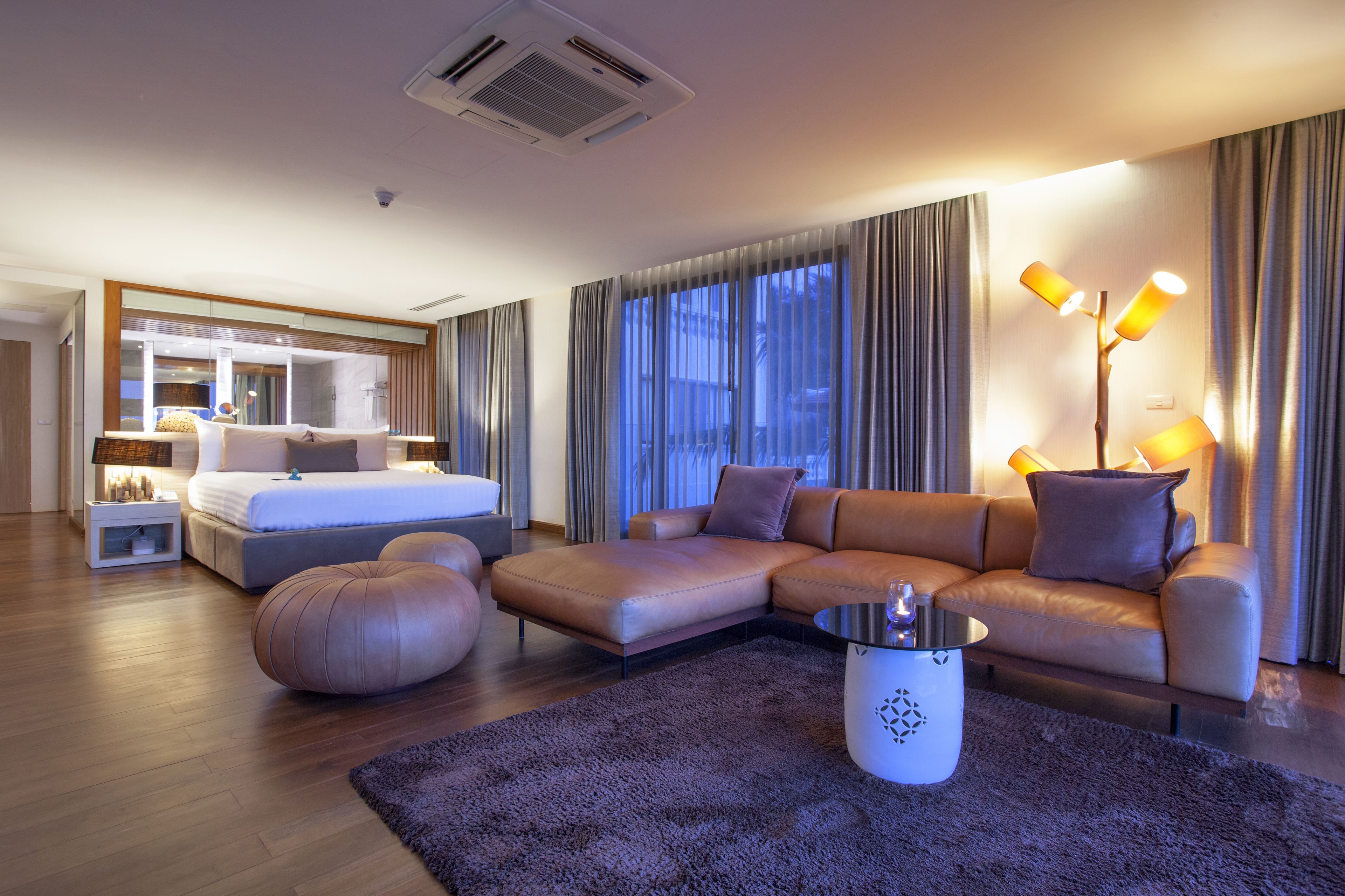 A modern hotel room with a bed, sofa, ottoman, and a coffee table.