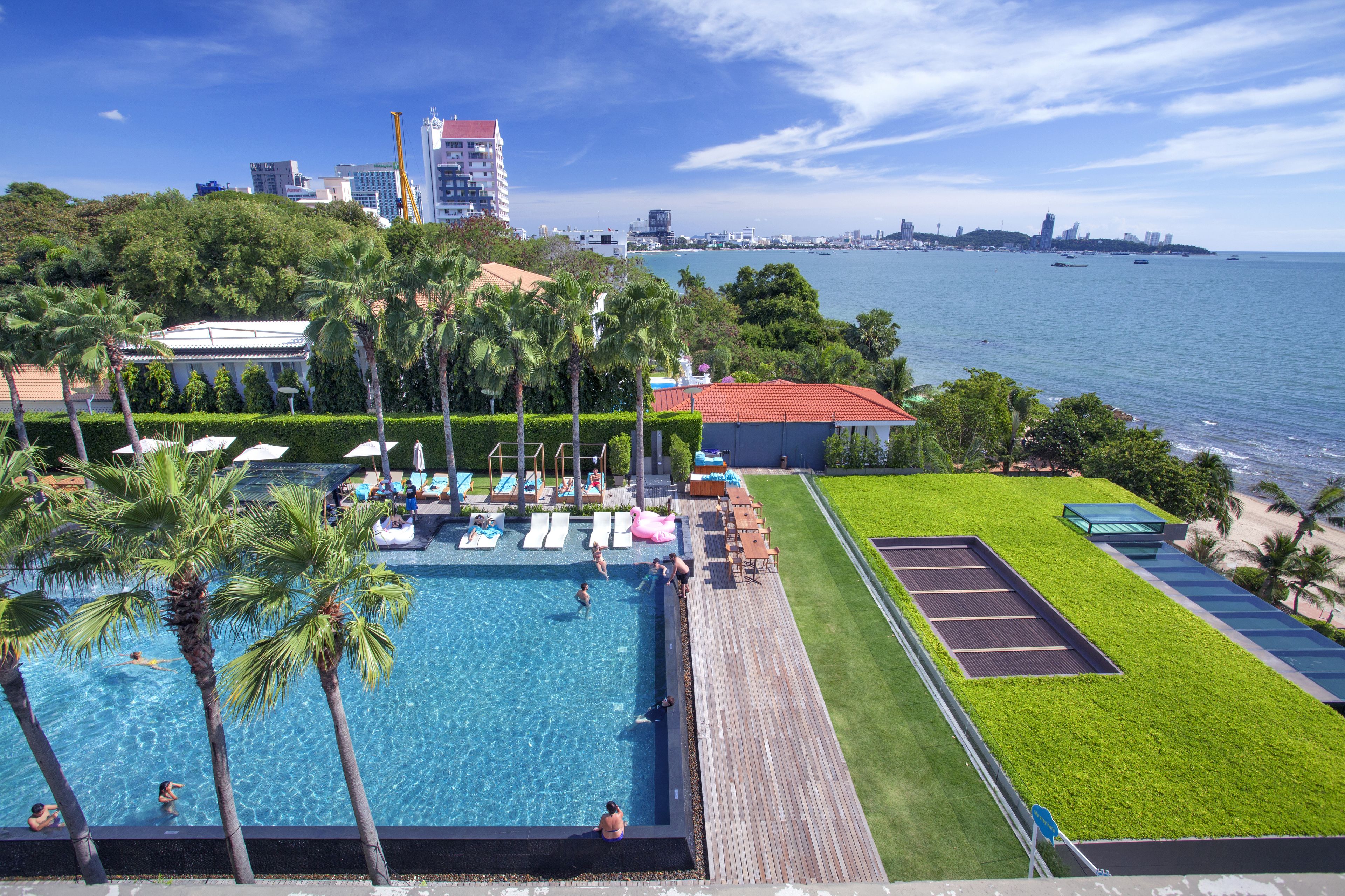 Una piscina en la azotea con palmeras, vista al mar y un horizonte urbano de fondo.