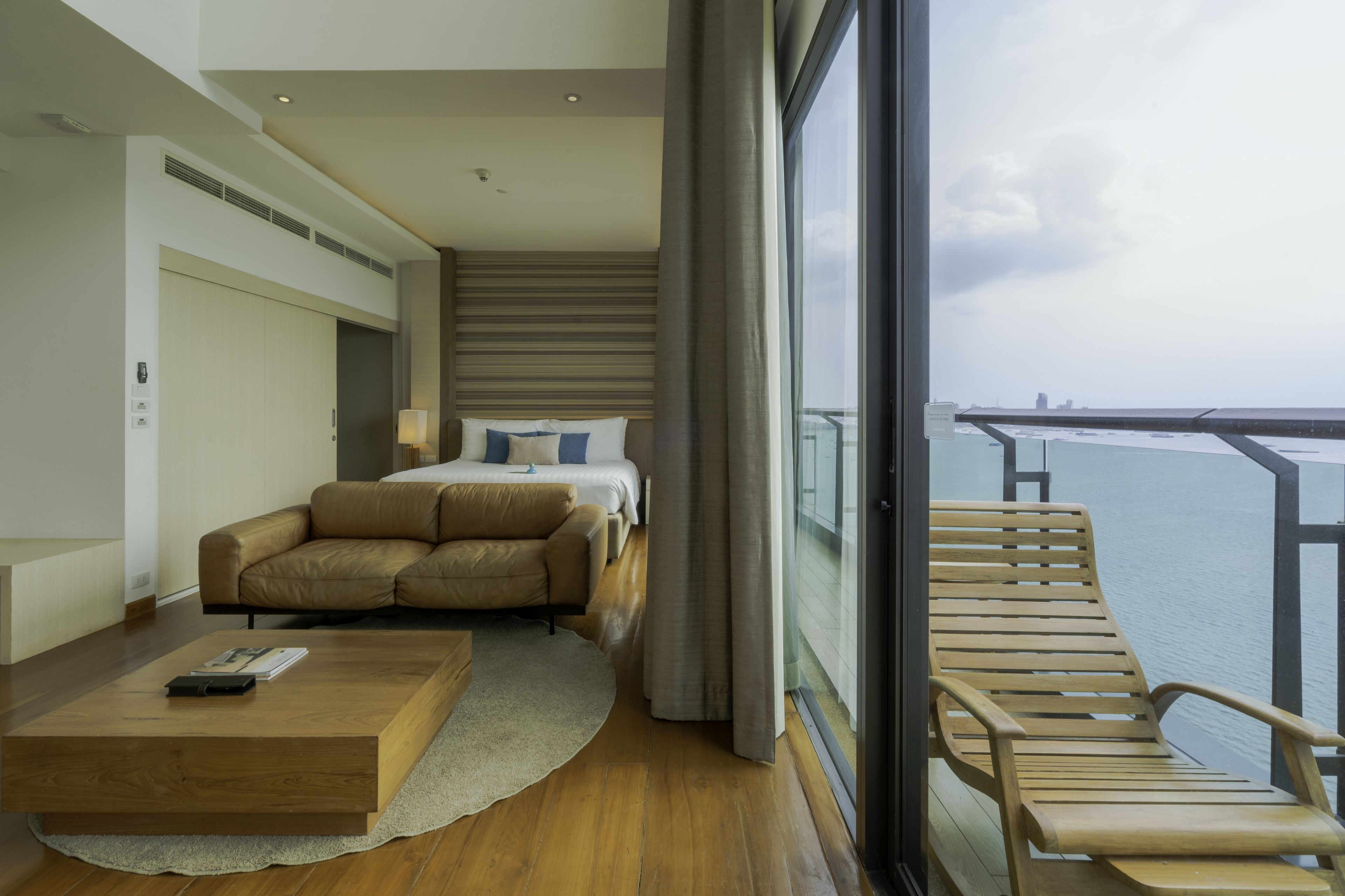 Una habitación de hotel moderna con una cama, un sofá, una mesa de centro de madera y un balcón con vista al mar.