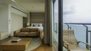 A modern hotel room with a bed, a sofa, a wooden coffee table, and a balcony with a view of the sea.