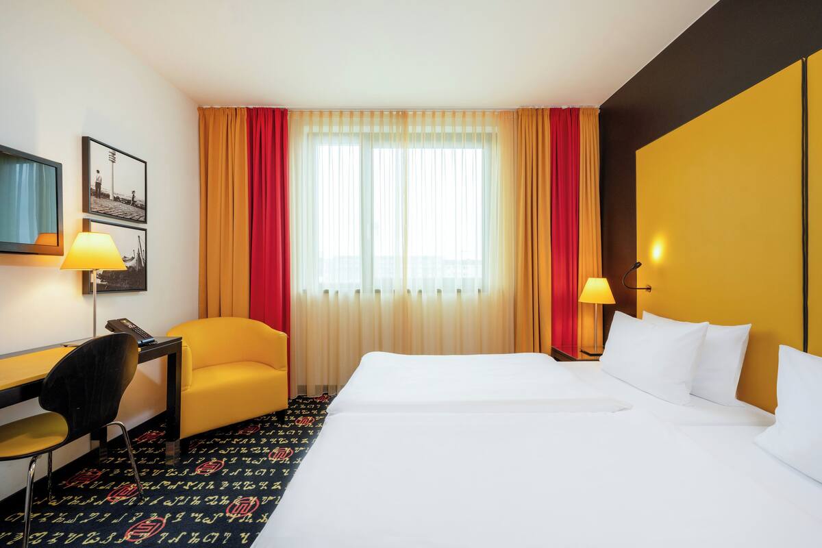 A hotel room with a bed, a desk, a chair, and a window with curtains.