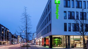 Un hotel moderno con un llamativo letrero verde, grandes ventanales y un área de entrada bien iluminada.