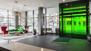 Un lobby moderno con una entrada iluminada en verde, ventanas amplias y mobiliario contemporáneo.