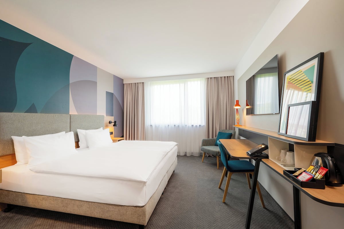 A hotel room with a large bed, a desk with a chair, a TV, and a window with curtains.
